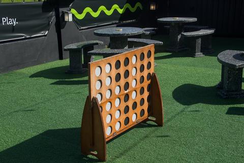 Giant wooden connect four frame with white and black discs on artificial grass, four-in-a-row game