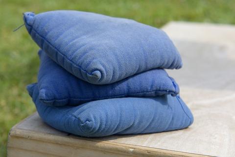Stack of blue fabric toss bags resting on a wooden board outdoors on grass, cornhole