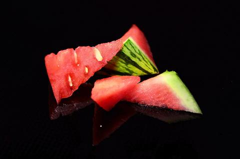 Juicy red watermelon wedges with green rind on a black reflective surface, Fruit Slash