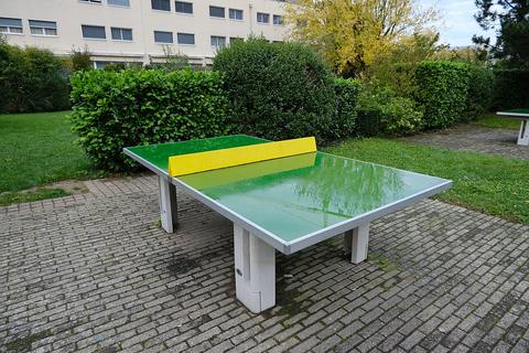 Green outdoor concrete table tennis table with a yellow net barrier on a paved courtyard, table tennis
